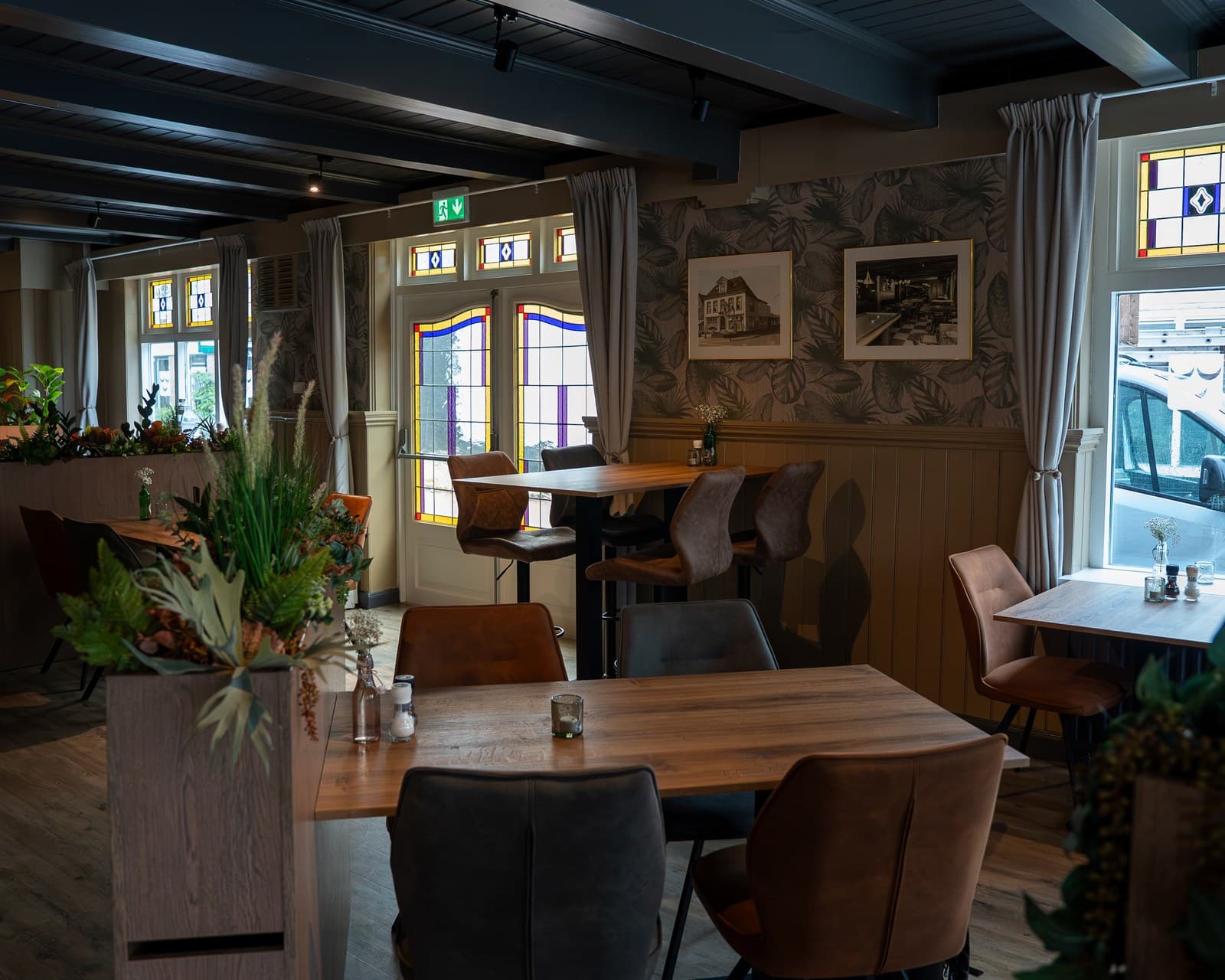 The warm interior of Het Wapen van Obdam featuring stained-glass windows and historic photography